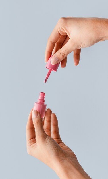 Manos de primer plano sosteniendo esmalte de uñas rosa