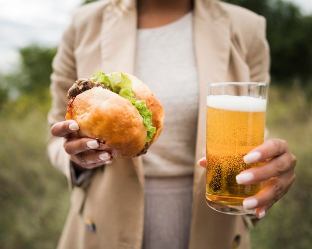 Manos de primer plano sosteniendo hamburguesa y cerveza