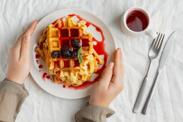 Manos de primer plano sosteniendo el plato con waffles