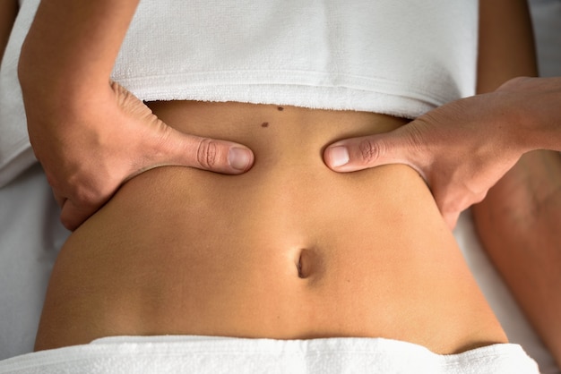 Manos que dan masajes al abdomen femenino. Terapeuta que aplica la presión en el vientre.