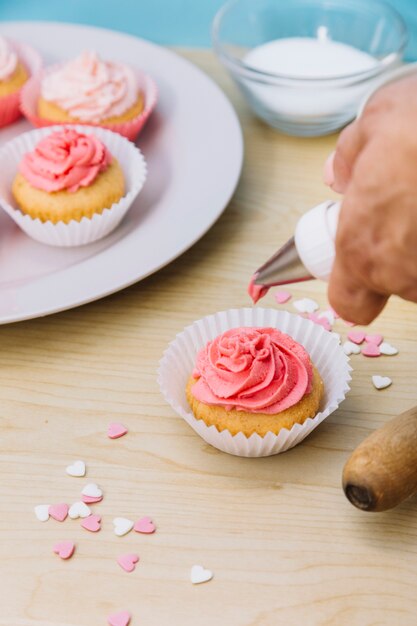 Manos que sostienen la bolsa de tubería llena de glaseado de crema decorando pastelitos