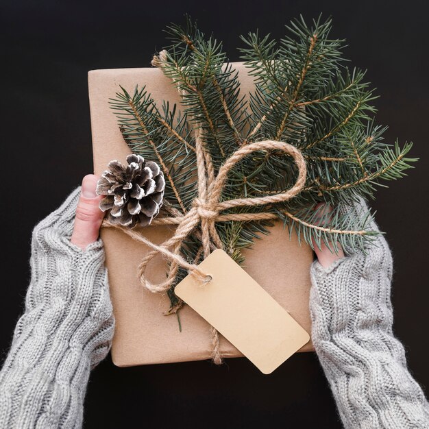 Manos que sostienen la caja de regalo decorada con gancho y ramitas de abeto