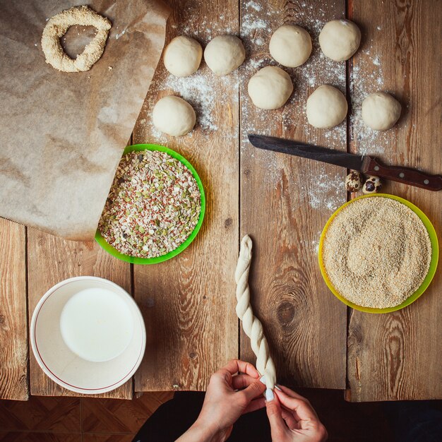 Manos que tuercen la masa para preparar el bagel turco simit vista superior.