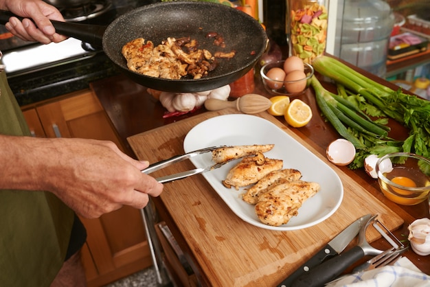 Manos recortadas de un cocinero anónimo transfiriendo carne frita con pinzas