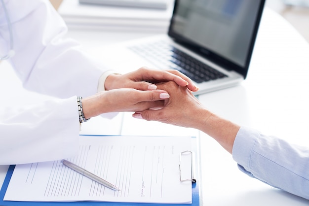 Manos recortadas del médico consolando a un paciente irreconocible