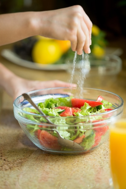 Manos salando una ensalada verde