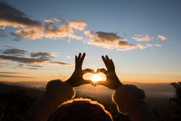 Manos de silueta formando una forma de corazón con la salida del sol