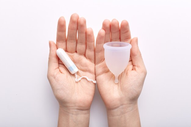 Manos sosteniendo artículos de higiene producidos para mujeres durante los períodos menstruales, con copa menstrual y tampón