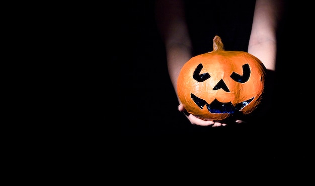 Manos sosteniendo calabaza decorativa de Halloween con cara tallada