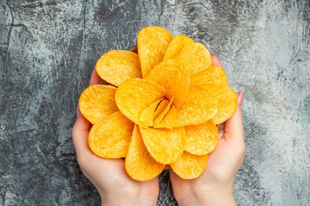 Manos sosteniendo deliciosas patatas fritas crujientes caseras en un recipiente marrón sobre mesa gris