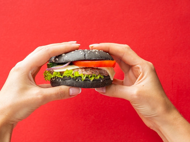 Manos sosteniendo una hamburguesa sobre fondo rojo