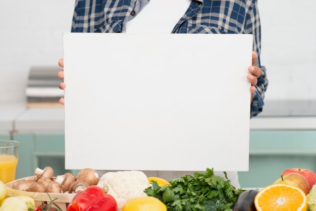 Manos sosteniendo maqueta cartel junto a verduras