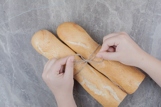 Manos sosteniendo un medio corte de pan baguette francés sobre superficie de mármol