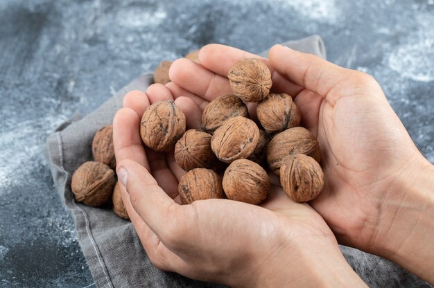 Manos sosteniendo muchas nueces saludables sobre una superficie de mármol.