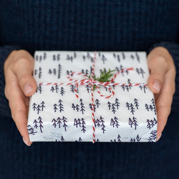 Foto gratuita manos sosteniendo el regalo de navidad con cadena y hoja de caramelo