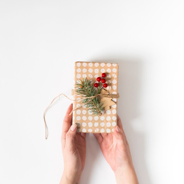 Manos sosteniendo el regalo de Navidad decorado con ramita de abeto