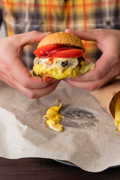 Foto gratuita manos sosteniendo una sabrosa hamburguesa con queso