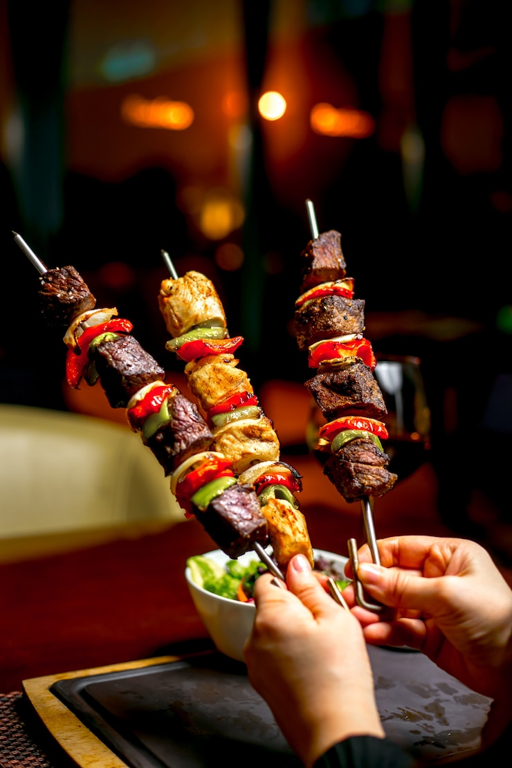 Foto gratuito manos sosteniendo shish kebab con coloridos pimientos