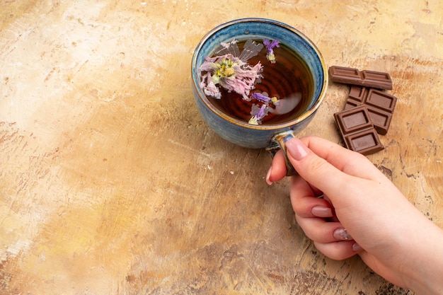 Manos sosteniendo una taza de té de hierbas caliente y barras de chocolate en la tabla de colores mezclados