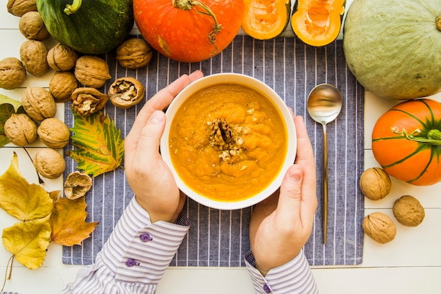 Manos sosteniendo el tazón con sopa de calabaza