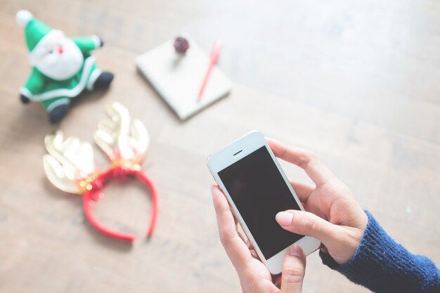 Manos sosteniendo el teléfono móvil con el fondo de la decoración de la Navidad, espacio de la copia