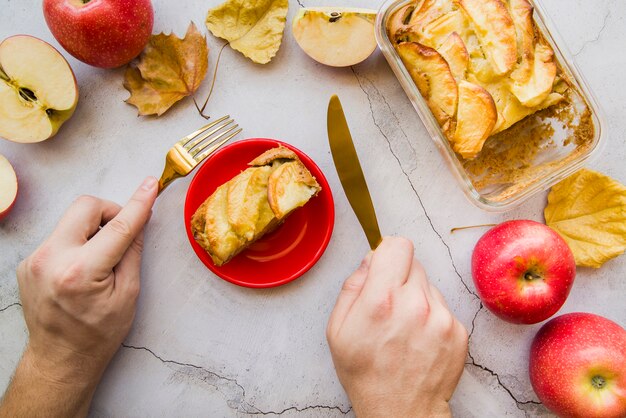 Manos sosteniendo el tenedor y el cuchillo por encima de la tarta de manzana