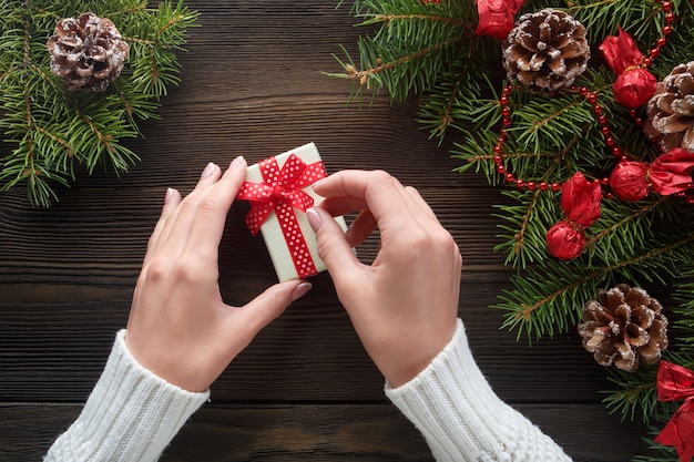 Manos sujetando una caja blanca de regalo con pino alrededor