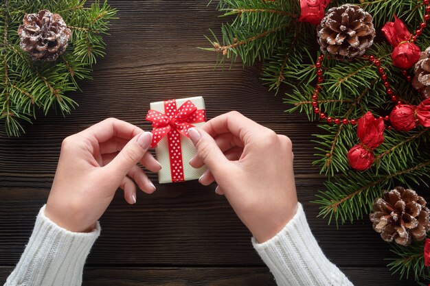 Manos sujetando una caja blanca de regalo con pino alrededor