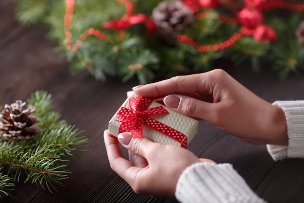 Manos sujetando una caja de regalo con un pino con piñas de fondo