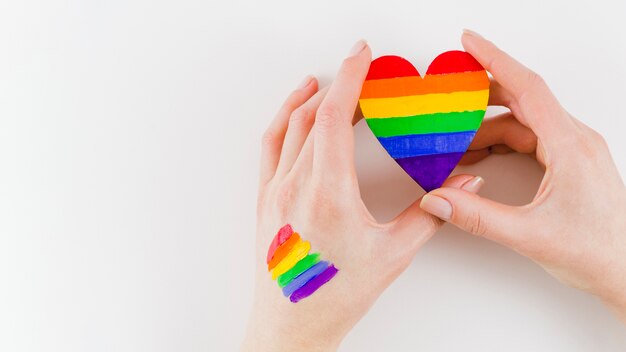 Manos sujetando un corazón con los colores de la bandera del orgullo