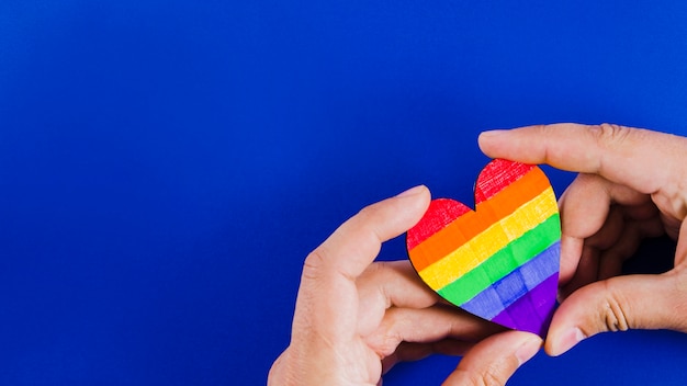 Manos sujetando un corazón con los colores de la bandera del orgullo