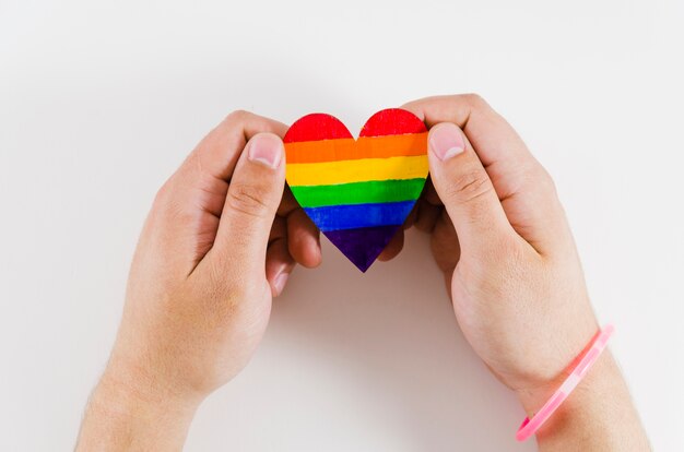 Manos sujetando un corazón con los colores de la bandera del orgullo