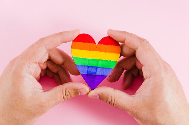 Manos sujetando un corazón con los colores de la bandera del orgullo