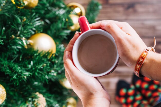 Manos sujetando taza de café al lado de árbol de navidad