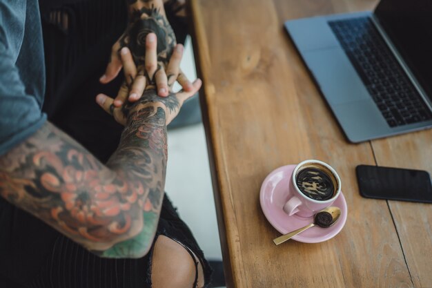 manos tatuadas, café y computadora portátil