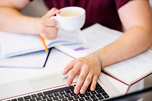 Manos con taza y computadora portátil en la mesa