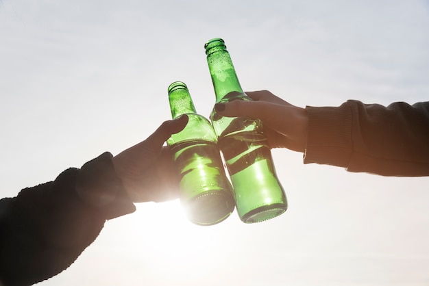 Manos tintineando botellas de cerveza.