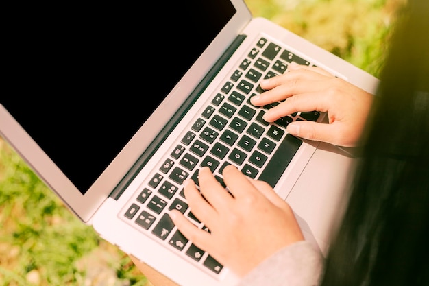 Manos del trabajador escribiendo en la computadora portátil en la naturaleza en un día soleado