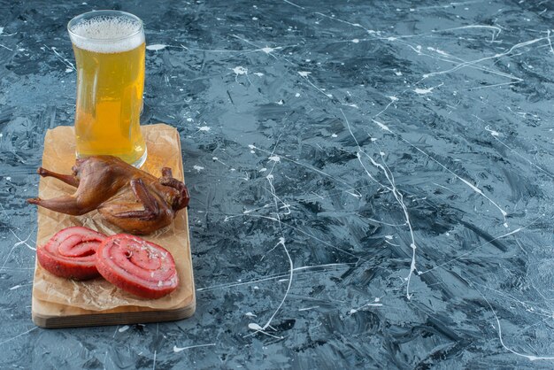 Manteca de cerdo, parrilla y cerveza en una tabla para cortar, sobre la mesa azul.