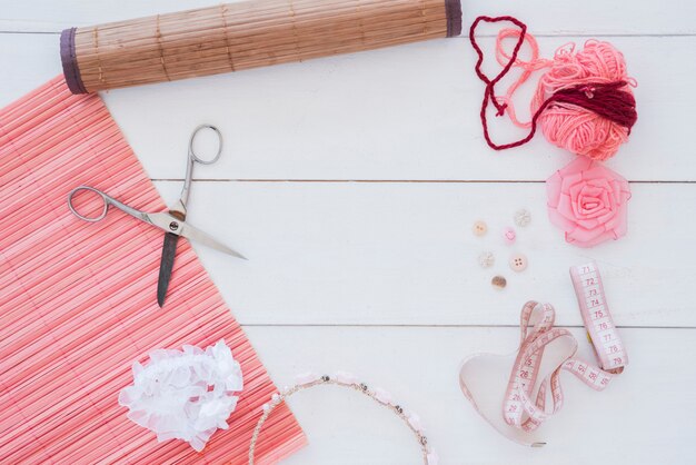Mantel de bambú; cortar con tijeras; lana; cinta rosa banda para el cabello; Botón y cinta métrica en el escritorio de madera.