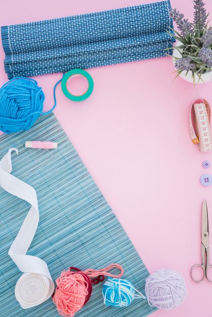 Mantel cinta; cortar con tijeras; carrete; cinta métrica; Botón y lana sobre fondo rosa.