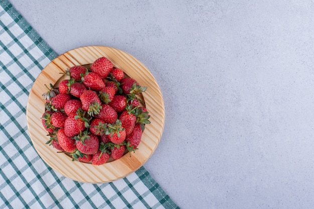 Mantel doblado debajo de una bandeja con un montón de fresas sobre fondo de mármol. Foto de alta calidad