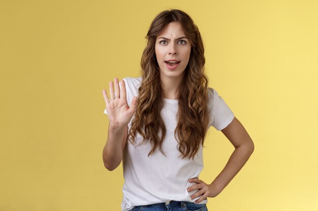 Mantenlo alto. Chica que se siente intensa y seria demanda de muecas terminar una conversación desagradable elevar el rechazo de la palma rechazo prohibir lo suficiente perder el tiempo frunciendo el ceño decepcionado fondo amarillo.