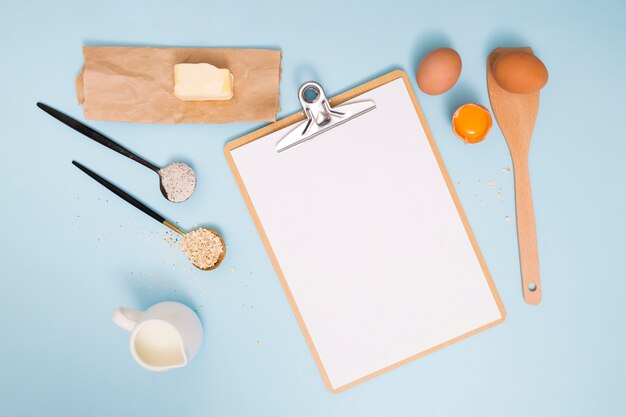 Mantequilla; huevos; harina; salvado de avena y leche con portapapeles sobre fondo azul