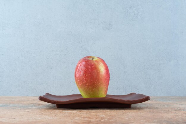 Una manzana dulce roja entera en un plato oscuro