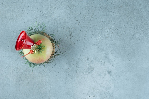 Una manzana fresca con campana de Navidad roja sobre mármol.