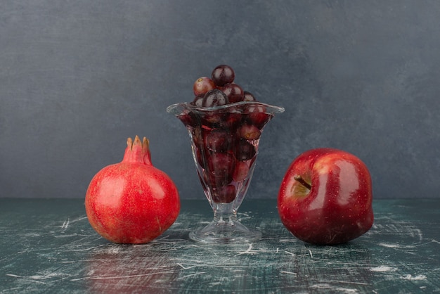 Manzana, granada y copa de uvas negras sobre mesa de mármol