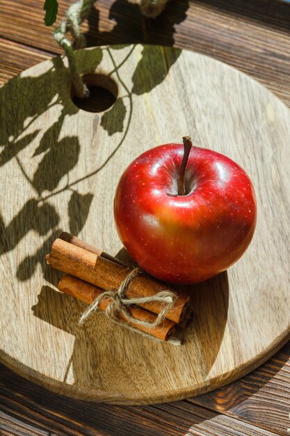 Manzana con hojas, palitos de canela sobre tabla para cortar madera