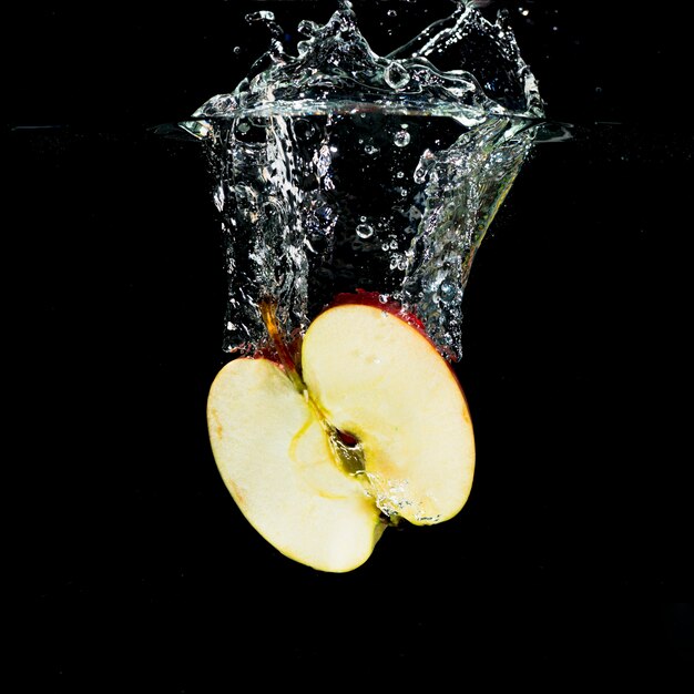 Manzana a la mitad fresca con salpicaduras de agua sobre fondo negro