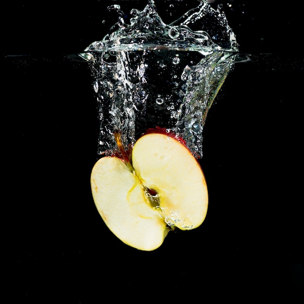 Manzana a la mitad fresca con salpicaduras de agua sobre fondo negro